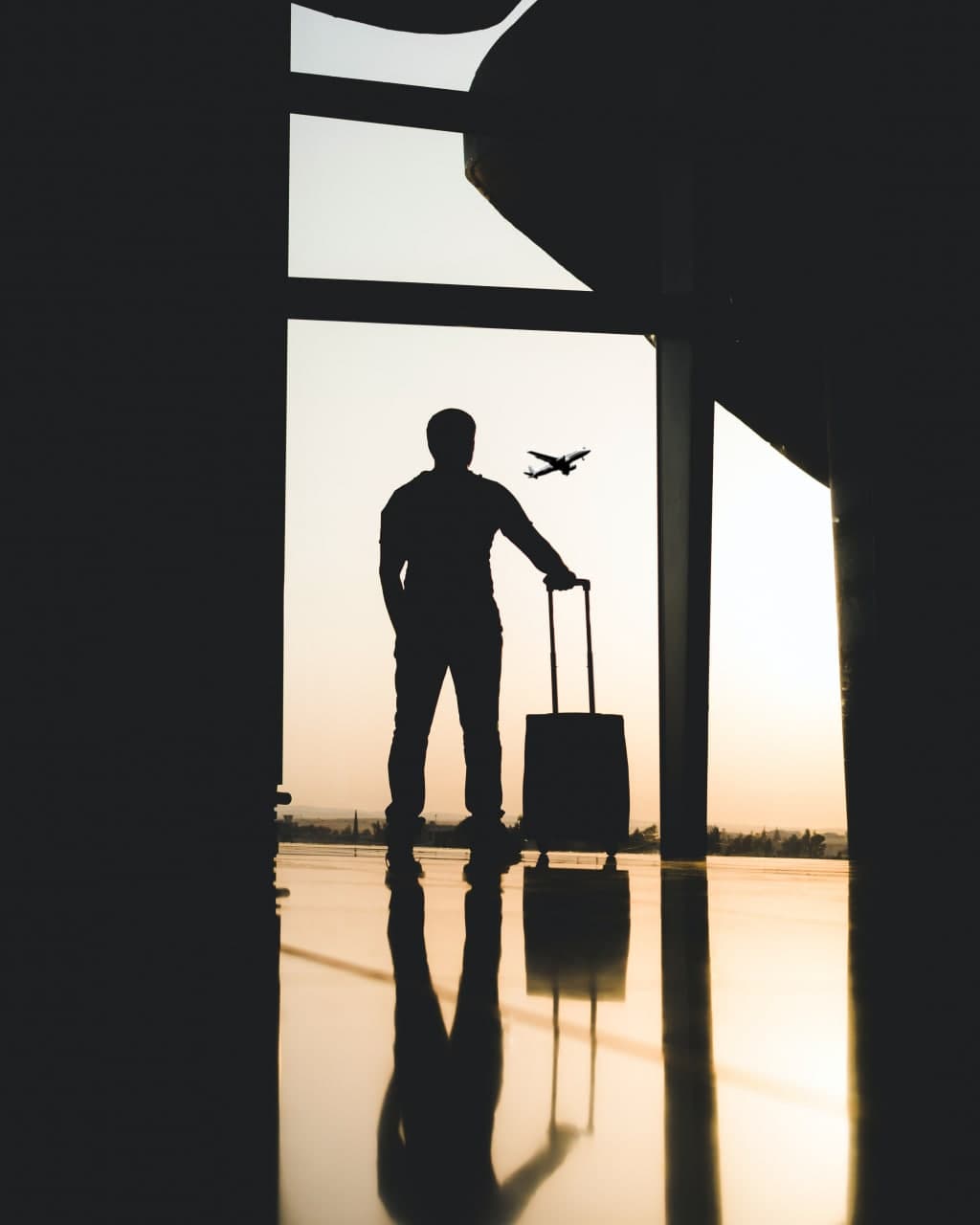 Muž s kufrem se dívá z okna na letišti směrem k letadlu.
